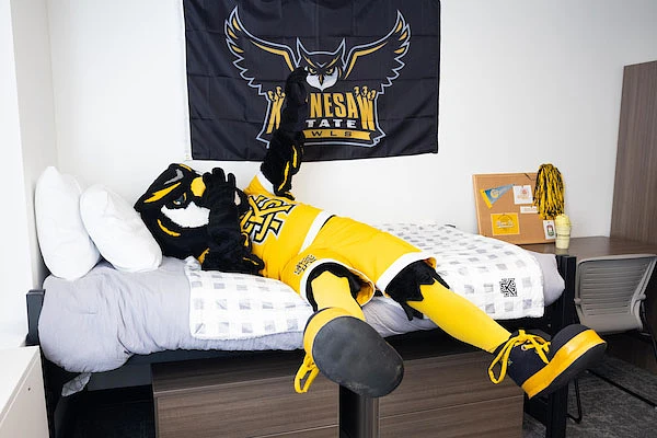 An owl mascot laying on a dorm bed