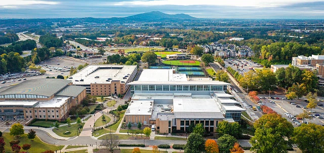 Tan buildings fill an image with grass fields and paved walkways between each one and parking lots and trees in the distance