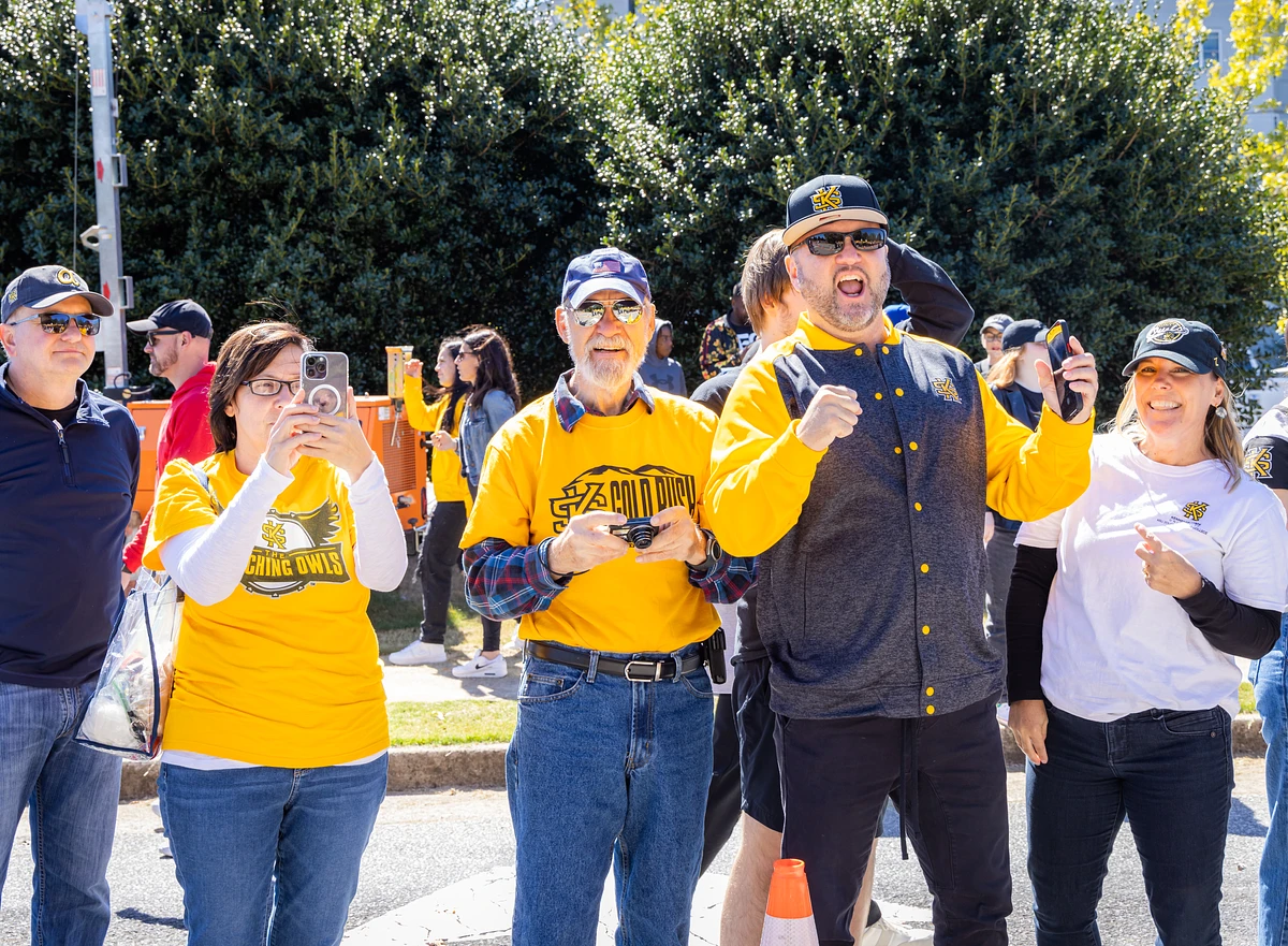 A group of people in yellow and black apparel enthusiastically cheer and take photos at an outdoor event.