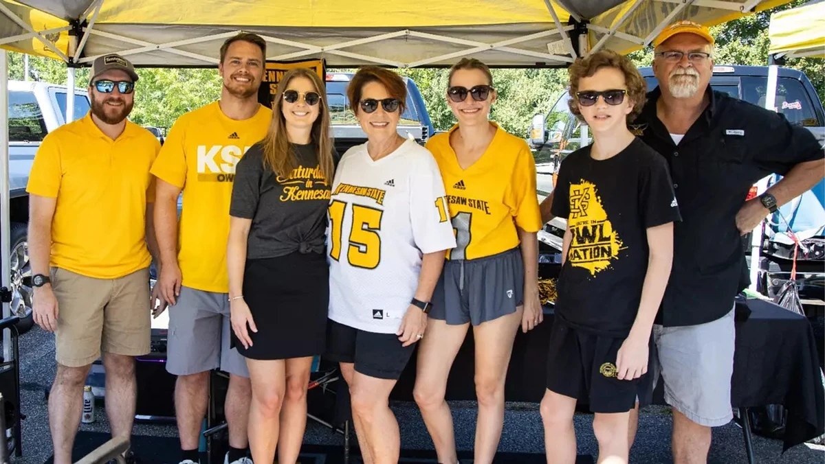 A group of people wearing Kennesaw State University attire pose under a yellow tent.